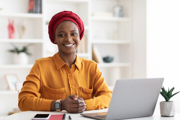 Muslim african american woman posing at office, working on laptop