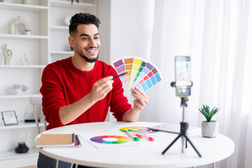 Cheerful millennial muslim guy designer with beard points to color palettes to client and shoots...