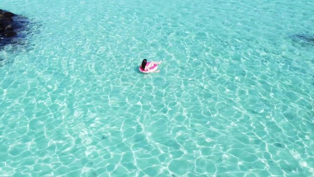 Woman in bikini rests on inflatable swimming ring donut in a pool with blue water. Concept of travel, vacation, weekends, holidays at sea Maldives