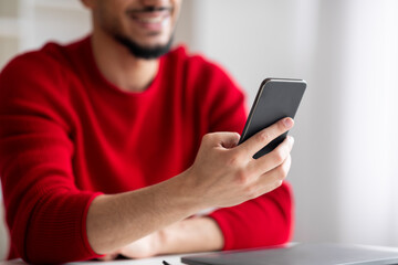 Cropped smiling young islamic man with beard typing on smartphone in home office interior