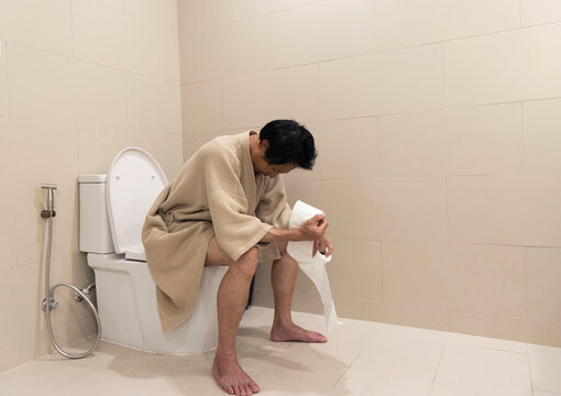 Man sitting in the toilet bowl. In the bathroom which he is unhappy with constipation, diarrhea concept