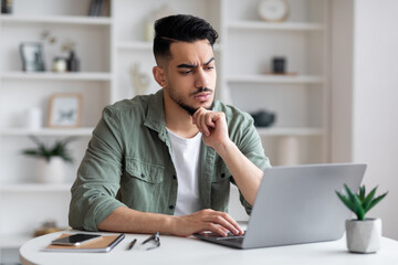 Obraz premium Thoughtful concentrated sad young arabic man with beard typing on laptop and have problem with job