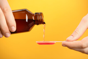 Woman pouring cough syrup into dosing spoon on orange background, closeup