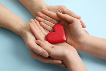Obraz premium Young and elderly women holding red heart on light blue background, closeup