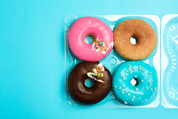 Obraz na płótnie Canvas Box of delicious donuts on light blue background, top view. Space for text