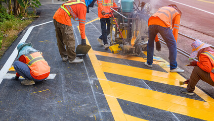 Road workers group with thermoplastic spray marking machine are painting yellow traffic sign on...