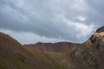 Dramatic alpine landscape with wide sharp mountain ridge under gray cloudy sky. Dark atmospheric mountain scenery with large sharp rocks on ridge top under rainy clouds in gray sky at overcast weather