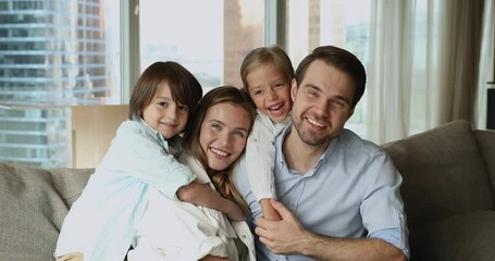 Beautiful wellbeing family portrait, travel and holidays at rented accommodation, medical insurance cover concept. Happy homeowners couple their preschool children sit on sofa smiling look at camera