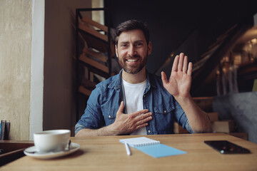 Handsome man with hand on chest, making oath promise gesture in cafe. Promissing concept. Portrait.