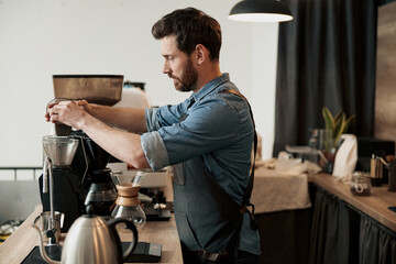 Barista pours coffee beans into the coffee machine tank for grinding standing behind counter