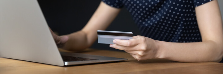 Close up of female hand with credit card, laptop over work table. Cropped banner shot. Bank customer woman shopping on Internet stores, making online payment, international transactions