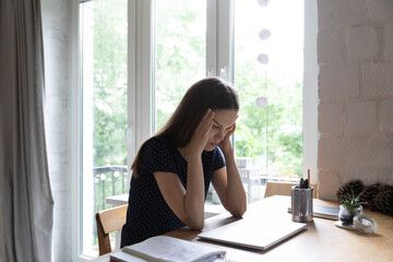 Shocked tired student girl holding head, touching temples, suffering from headache at work table...