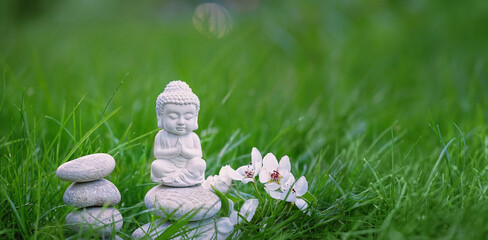 Buddha statue and spa stones, flowers in green grass, natural abstract summer background. Buddhism culture symbol. esoteric spiritual practice, soul relax, meditation. harmony, life balance concept.