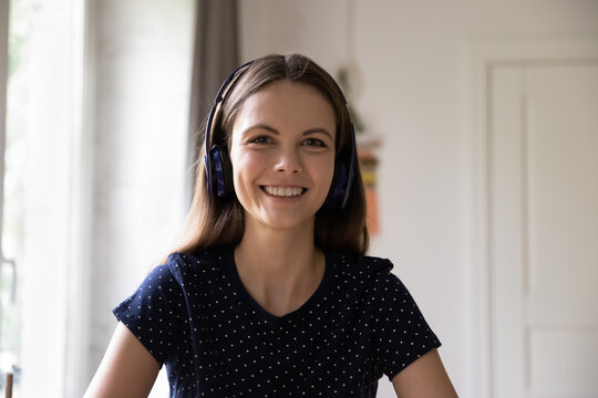 Cheerful confident student, intern girl in wireless headphones head shot portrait. Positive young woman talking on video call, attending online conference, speaking, looking at camera