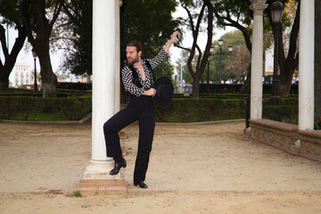 gypsy man dancing flamenco with long hair and beard in a park next to some marble columns. He is...
