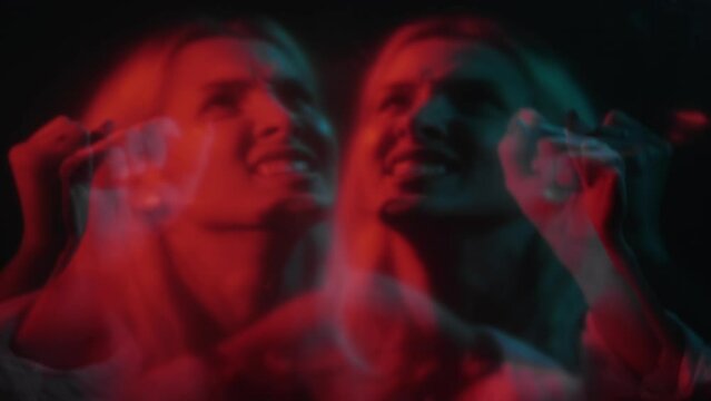 Scary horror. Spooky night. Screaming face. Defocused double exposure of afraid shouting trapped woman in red neon light on dark background.