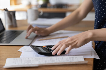 Young woman using calculator, laptop for paperwork, counting expenses, spending, analyzing domestic...