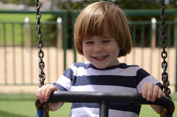 Happy little boy having fun on a swing outdoor. Positive boy having fun on a swing on the...