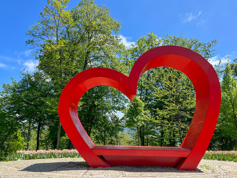 big red heart over green trees and beautiful blue sky in a sunny day at a park
