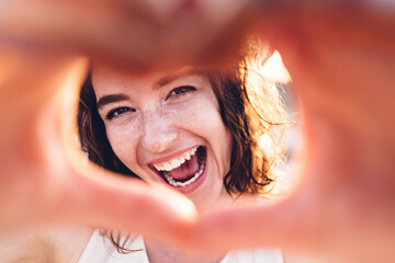 Close up image of smiling woman in swimwear on the beach making a heart shape with hands - Pretty...