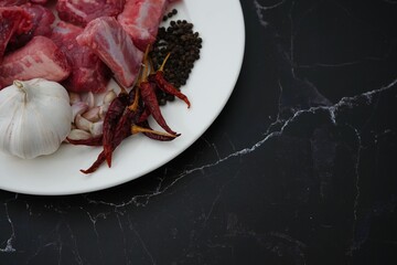 Image of meat, garlic, pepper and dried chilies in a white plate on a black background