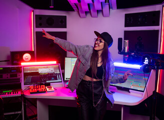 Beautiful stylish girl sound engineer in a recording studio with neon lights in a cap and glasses