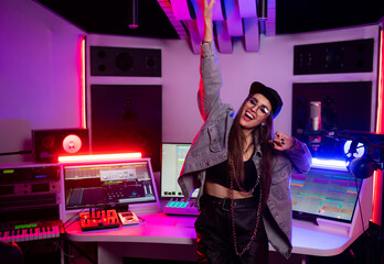 Beautiful stylish girl sound engineer in a recording studio with neon lights in a cap and glasses