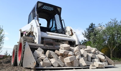 Skid steer loader for construction site with loading bucket filled with bricks. - obrazy, fototapety, plakaty
