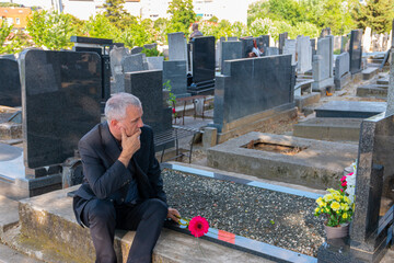 Mature man in black clothes on cemetery, holding a flower and Mourning for family loss. Concept for Death, Mourning, Funeral and Spirituality.