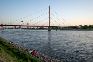 Outdoor scenery of people sit and enjoy nice atmosphere at promenade along riverside of Rhine River during evening sunset time in Düsseldorf, Germany.