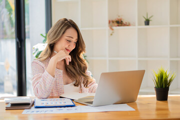 Asian businesswoman using her laptop calculator to make money on her desk math, tax, accounting, statistical reports, and analytical research ideas. Modern office real estate investment information