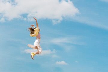 Girl during jump in the sky. Woman jumping through the air in front of beautiful cloudy sky....