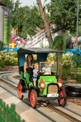 Amusement park. Young mother and two children ride in small car. Nanny rides with children in the park.