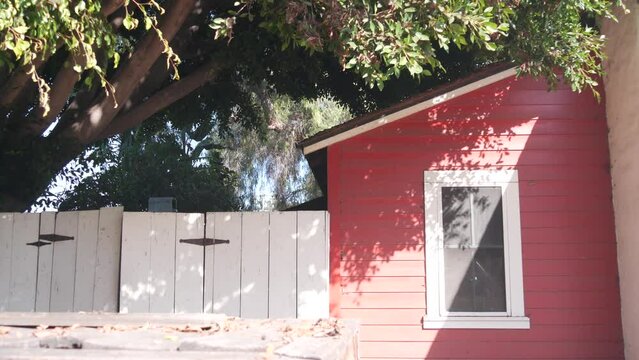 Red wooden rural ranch house, rustic building exterior, window and gate under tree, California, USA. Provincial homestead architecture, facade of retro farm in country village. Countryside dwelling.
