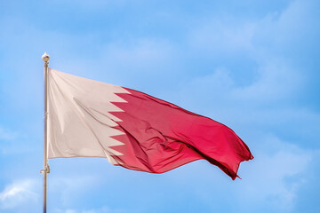 National flag of Qatar is flying in the wind against the blue sky. Close-up