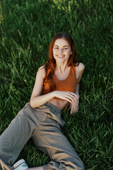 View from above a woman lying on the grass smiling and looking into the cameras happy lifestyle in the park on the green grass in the sunset light