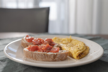 Two toasts with cream cheese and salmon and omelet on white plate