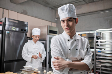 Portrait of young Asian male chef in white cooking uniform looking at the camera, arms crossed with...