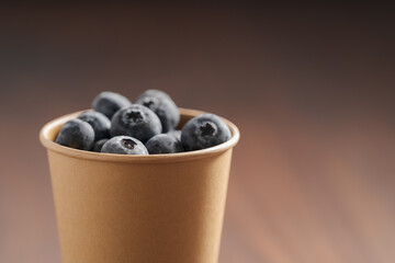 Fresh organic blueberries in papaer cup on wood table with copy space