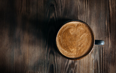 A cup of freshly brewed coffee with fresh milk foam stands on a brown wooden table.