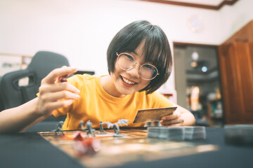Happy young adult asian woman playing board game on top table at home