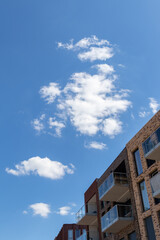 Part of an apartment building against a clear blue sky with a few white clouds in an abstract setting.
