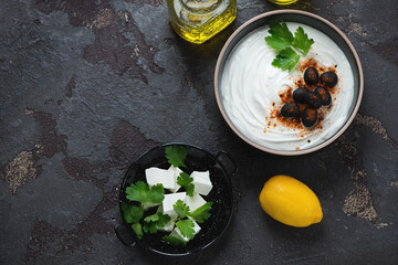 Bowl of greek feta dip topped with black olives and paprika, flat lay on a brown stone background,...