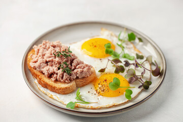 Breakfast - fried eggs and a sandwich with goose pate in a plate on the table