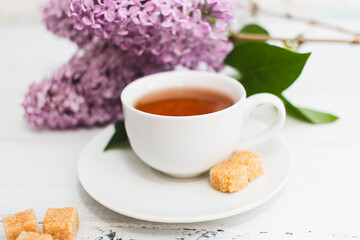 Obraz na płótnie Canvas Cup of tea and flowers of a lilac on a white wooden background