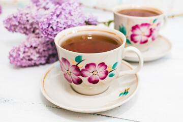 Fototapeta premium Cup of tea and flowers of a lilac on a white wooden background