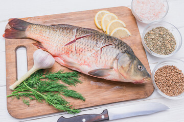 Fresh carp fish with incisions on the carcass lies on a cutting board with spices and seasonings