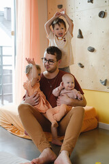 Obraz premium Happy father with tree small kids playing at home. Dad cuddling with children, holding them on hands. Fun in big family, sunny day. Daddy carry all children in him, laughing. Happy Fathers day