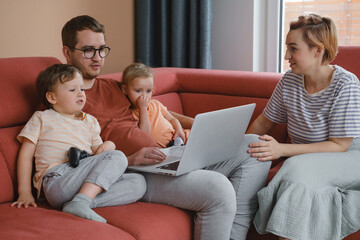 Big happy family watching movies playing games on laptop. Mother father kids spending time with gadgets on sofa Children with parents looking on computer screen at home Siblings playing with console