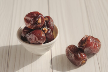 Dried dates in a white ceramic bowl in the bright sun. The edible fruit of the date palm, valued...